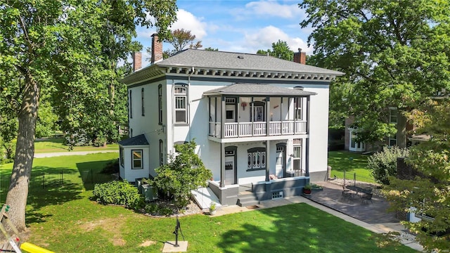 rear view of house with cooling unit, a balcony, fence, a yard, and a chimney