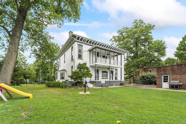 italianate home with a playground, a chimney, stucco siding, a balcony, and a front lawn