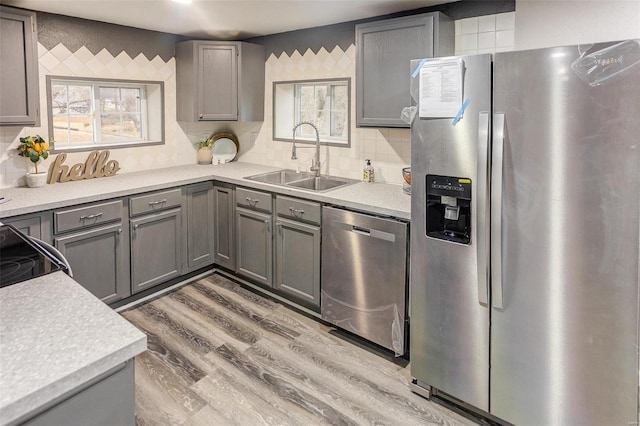 kitchen featuring appliances with stainless steel finishes, light countertops, a sink, and gray cabinetry