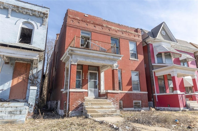 view of front of house with entry steps, brick siding, and a balcony