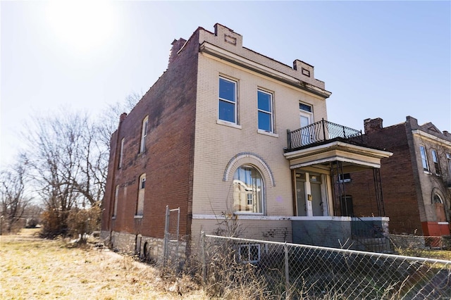 view of front of home with a balcony, a fenced front yard, and brick siding