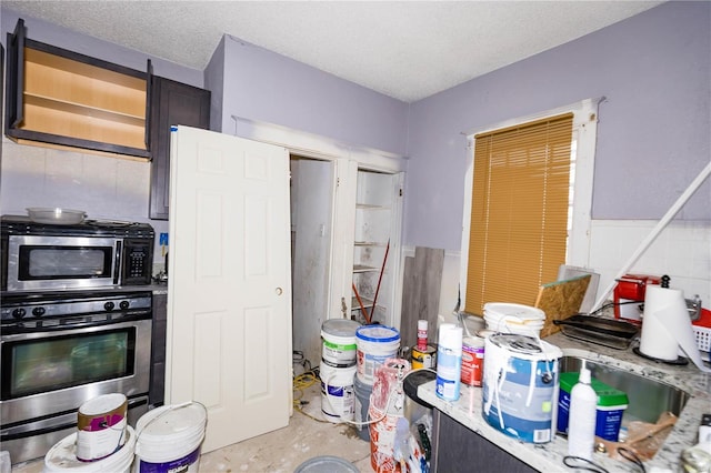 kitchen with a textured ceiling, stainless steel microwave, unfinished concrete flooring, and wall oven