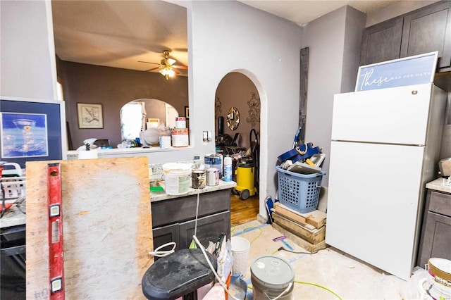 kitchen featuring ceiling fan, arched walkways, dark brown cabinetry, light countertops, and freestanding refrigerator