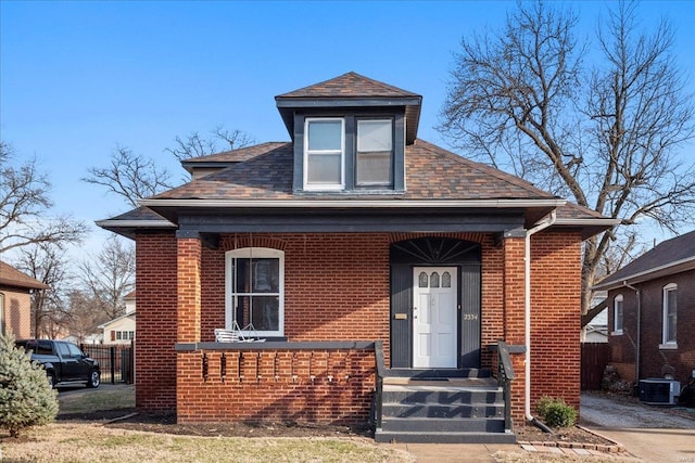 bungalow-style home with central air condition unit, roof with shingles, fence, and brick siding