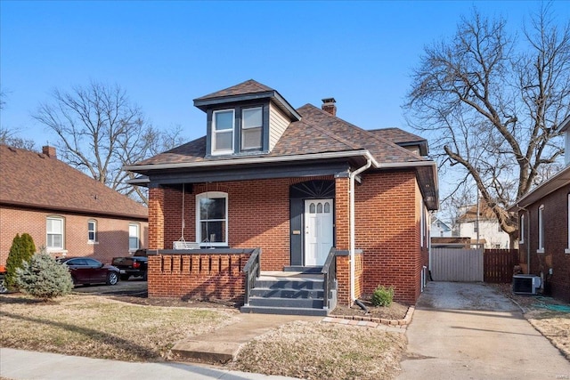 bungalow with brick siding, a chimney, a porch, a shingled roof, and central AC unit