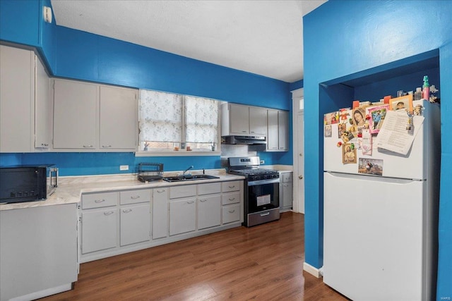 kitchen with stainless steel gas stove, freestanding refrigerator, light countertops, under cabinet range hood, and black microwave