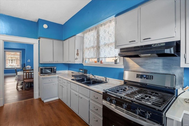 kitchen with dark wood finished floors, light countertops, appliances with stainless steel finishes, a sink, and under cabinet range hood