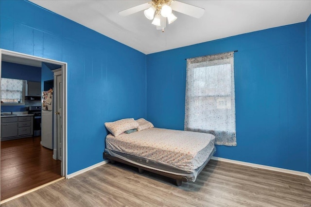 bedroom featuring baseboards, ceiling fan, wood finished floors, freestanding refrigerator, and a sink