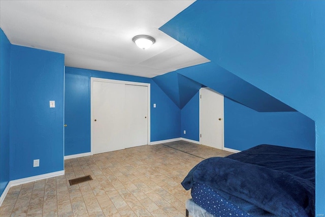 bedroom with baseboards, visible vents, vaulted ceiling, and a closet