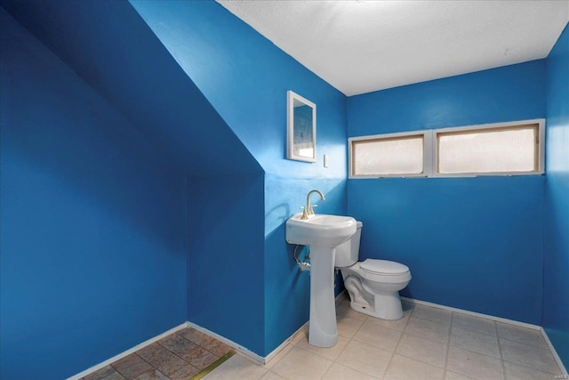 half bath with a textured ceiling, toilet, and baseboards