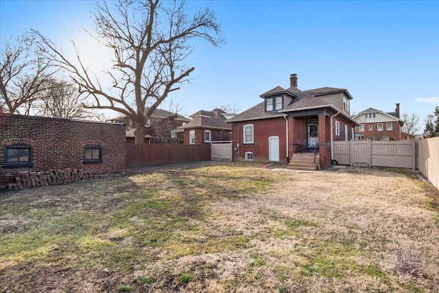 back of house with a yard, a fenced backyard, a chimney, and brick siding