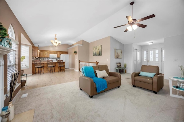 living area featuring vaulted ceiling, ceiling fan with notable chandelier, a fireplace, and light carpet