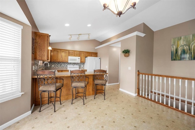 kitchen featuring lofted ceiling, a peninsula, white appliances, and baseboards