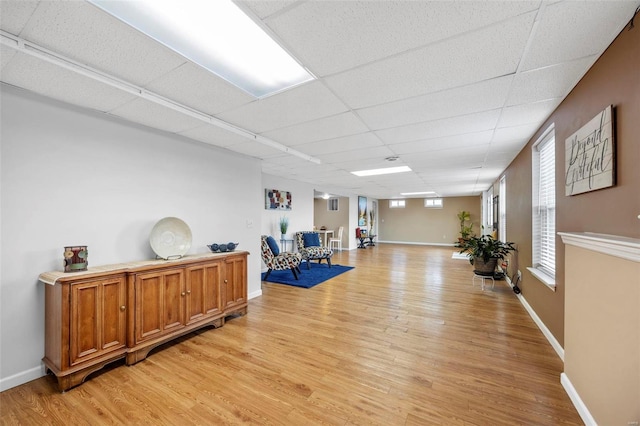 interior space featuring light wood-type flooring, a drop ceiling, and baseboards