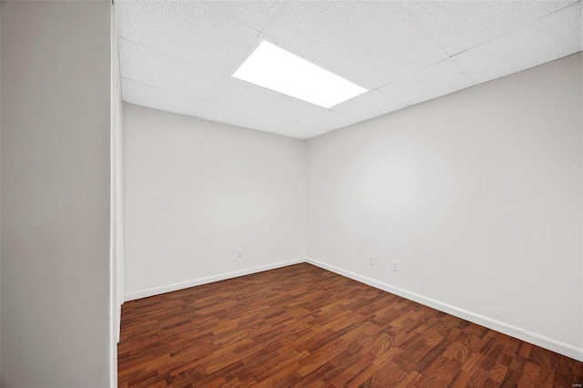 spare room with wood finished floors, a paneled ceiling, and baseboards