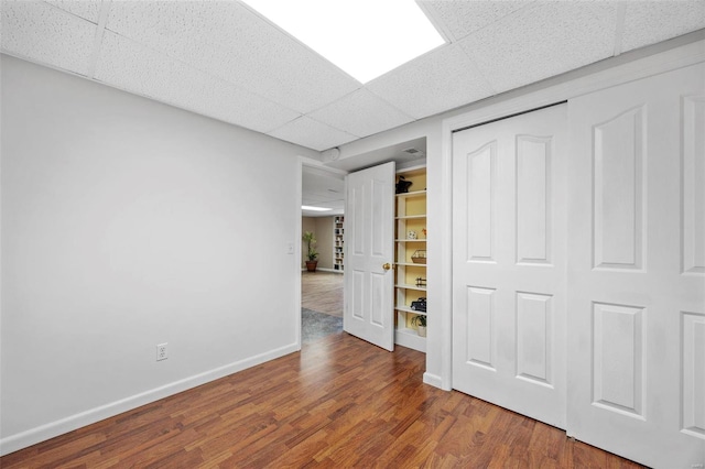 unfurnished bedroom featuring a paneled ceiling, a closet, baseboards, and wood finished floors