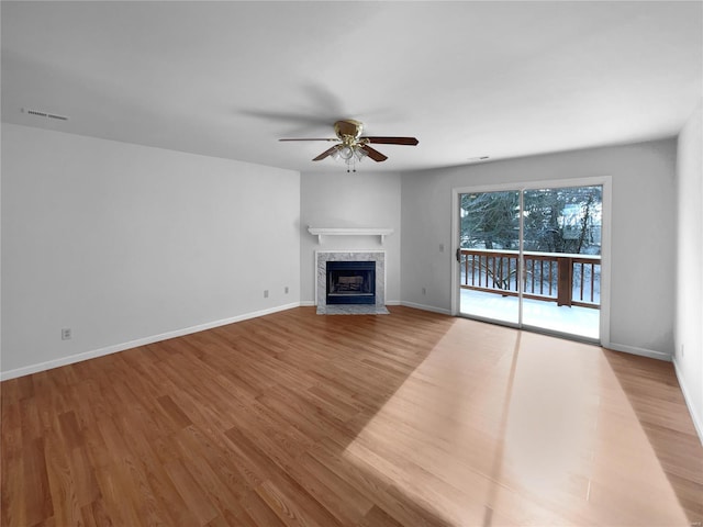 unfurnished living room featuring baseboards, visible vents, a ceiling fan, a premium fireplace, and wood finished floors