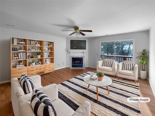 living area with a ceiling fan, a fireplace, visible vents, and wood finished floors