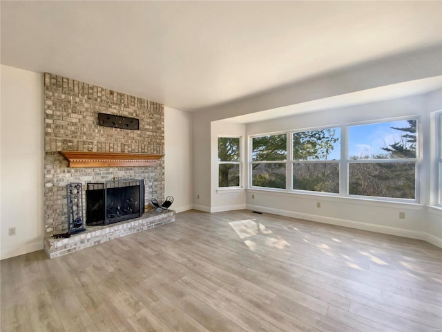 unfurnished living room featuring a brick fireplace, baseboards, and wood finished floors