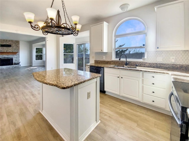 kitchen featuring dishwashing machine, a large fireplace, a sink, open floor plan, and a center island