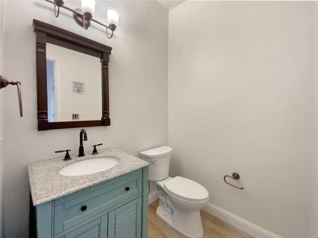 half bath featuring toilet, baseboards, wood finished floors, and vanity