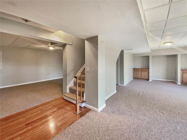 finished below grade area featuring carpet floors, a drop ceiling, baseboards, and stairs