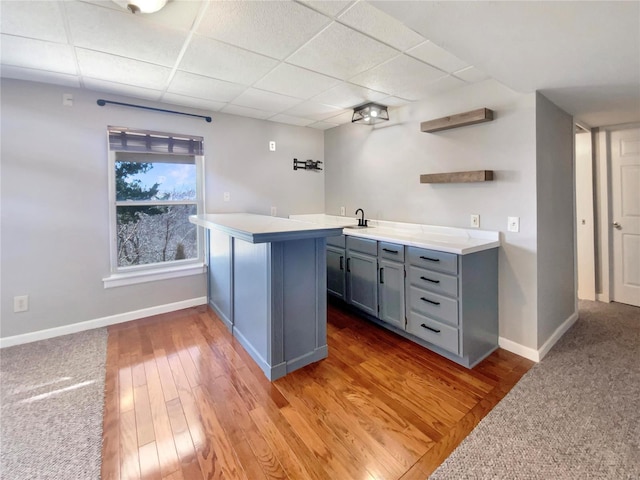 bar with a paneled ceiling, light wood finished floors, baseboards, and a sink