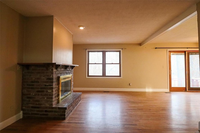 unfurnished living room with plenty of natural light, a brick fireplace, and wood finished floors