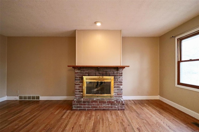 unfurnished living room with visible vents, baseboards, a brick fireplace, and wood finished floors