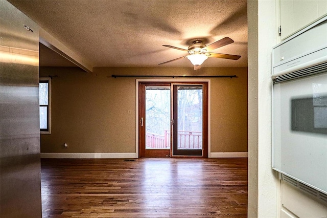 spare room with ceiling fan, dark wood-type flooring, baseboards, and a textured ceiling