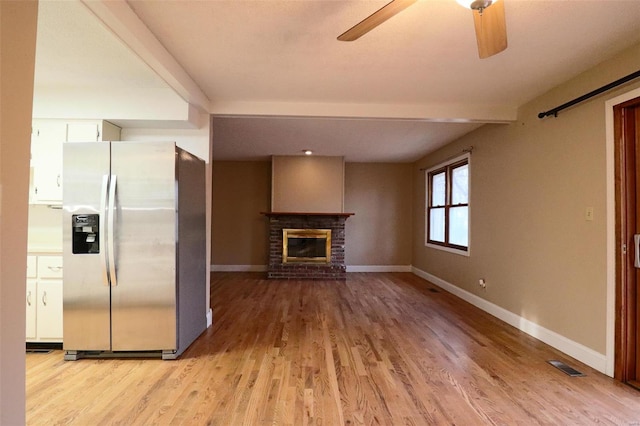 unfurnished living room featuring visible vents, a brick fireplace, baseboards, light wood-style floors, and a ceiling fan