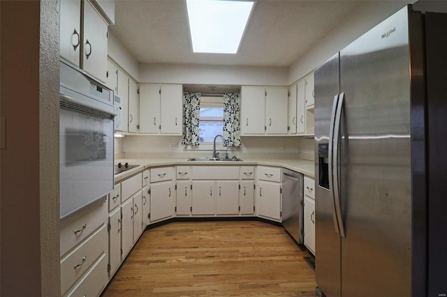 kitchen featuring light wood-style flooring, a sink, stainless steel appliances, light countertops, and white cabinets