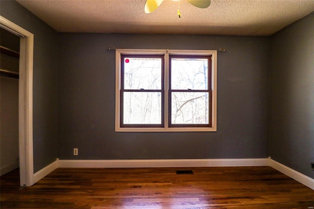 unfurnished bedroom featuring visible vents, a textured ceiling, baseboards, and dark wood-style flooring