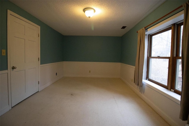 carpeted empty room with visible vents, a textured ceiling, a healthy amount of sunlight, and wainscoting