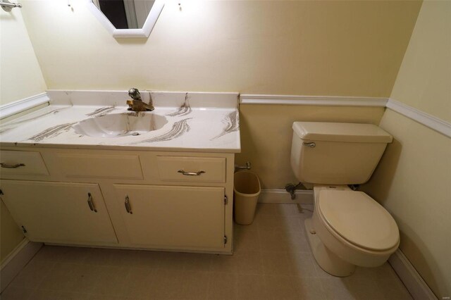 half bathroom featuring baseboards, toilet, and vanity