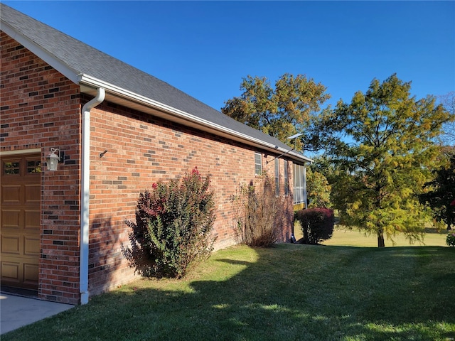 view of side of home featuring a yard, brick siding, and an attached garage