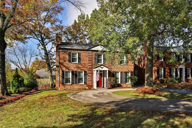 colonial-style house with brick siding, a front lawn, and a chimney