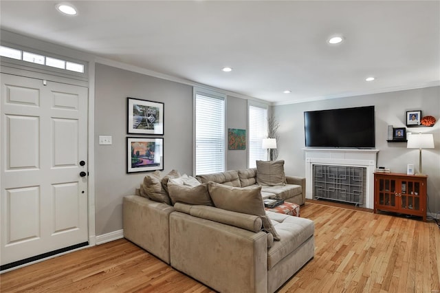 living area with light wood-type flooring, recessed lighting, crown molding, and a tile fireplace