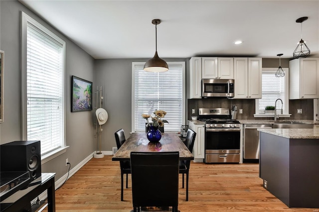 kitchen featuring appliances with stainless steel finishes, white cabinetry, light wood-style floors, and tasteful backsplash