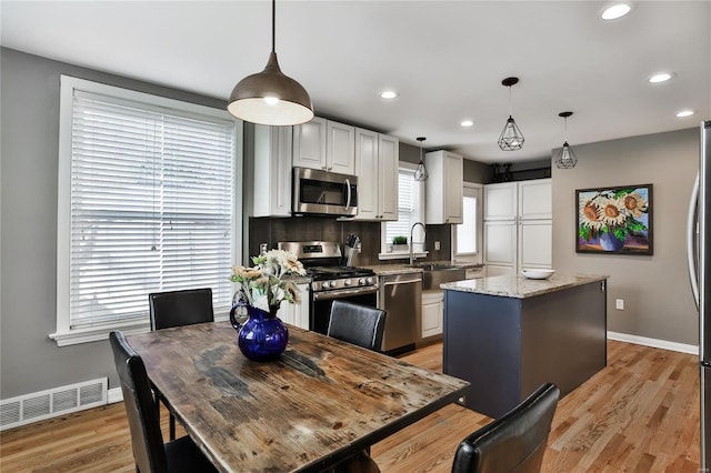 kitchen featuring visible vents, a kitchen island, appliances with stainless steel finishes, light wood-style floors, and a sink