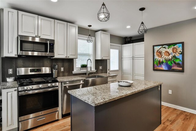 kitchen with tasteful backsplash, appliances with stainless steel finishes, light stone countertops, white cabinetry, and a sink