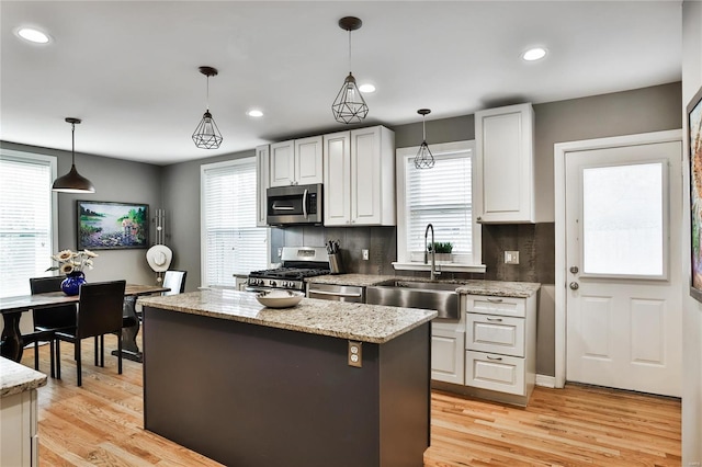 kitchen with light wood-type flooring, a kitchen island, appliances with stainless steel finishes, and a sink