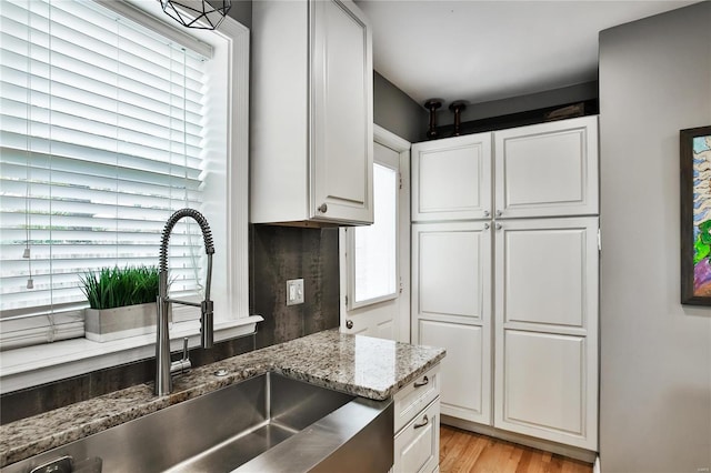 kitchen featuring light wood finished floors, a sink, white cabinets, and light stone countertops