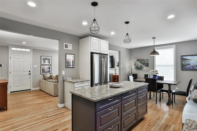 kitchen featuring light wood-type flooring, freestanding refrigerator, visible vents, and white cabinetry