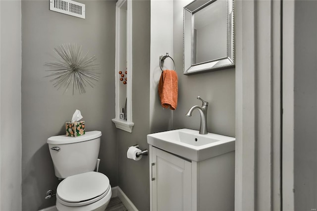 half bathroom featuring toilet, baseboards, visible vents, and vanity