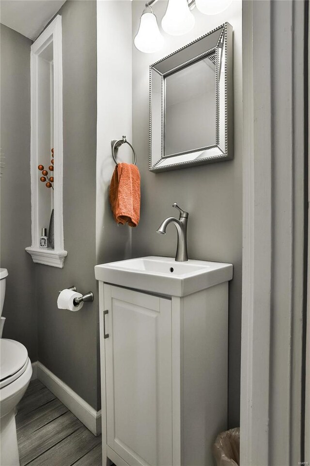 half bathroom featuring toilet, baseboards, wood finished floors, and vanity