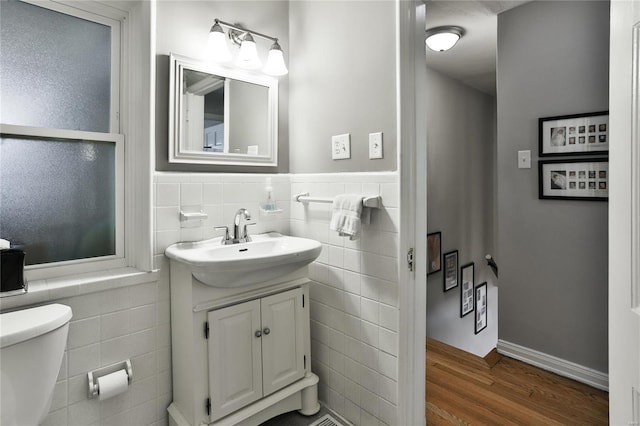 bathroom with toilet, a wainscoted wall, wood finished floors, vanity, and tile walls