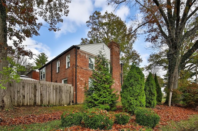 view of home's exterior featuring a chimney, fence, and brick siding