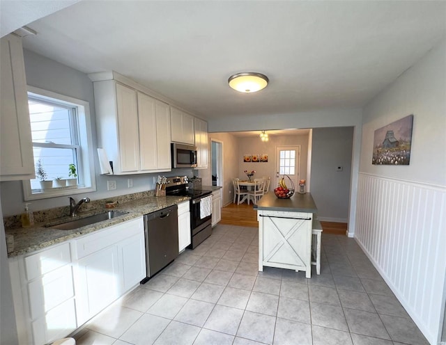 kitchen featuring light tile patterned floors, appliances with stainless steel finishes, wainscoting, white cabinetry, and a sink