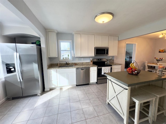 kitchen with a breakfast bar area, light tile patterned flooring, stainless steel appliances, a sink, and white cabinetry